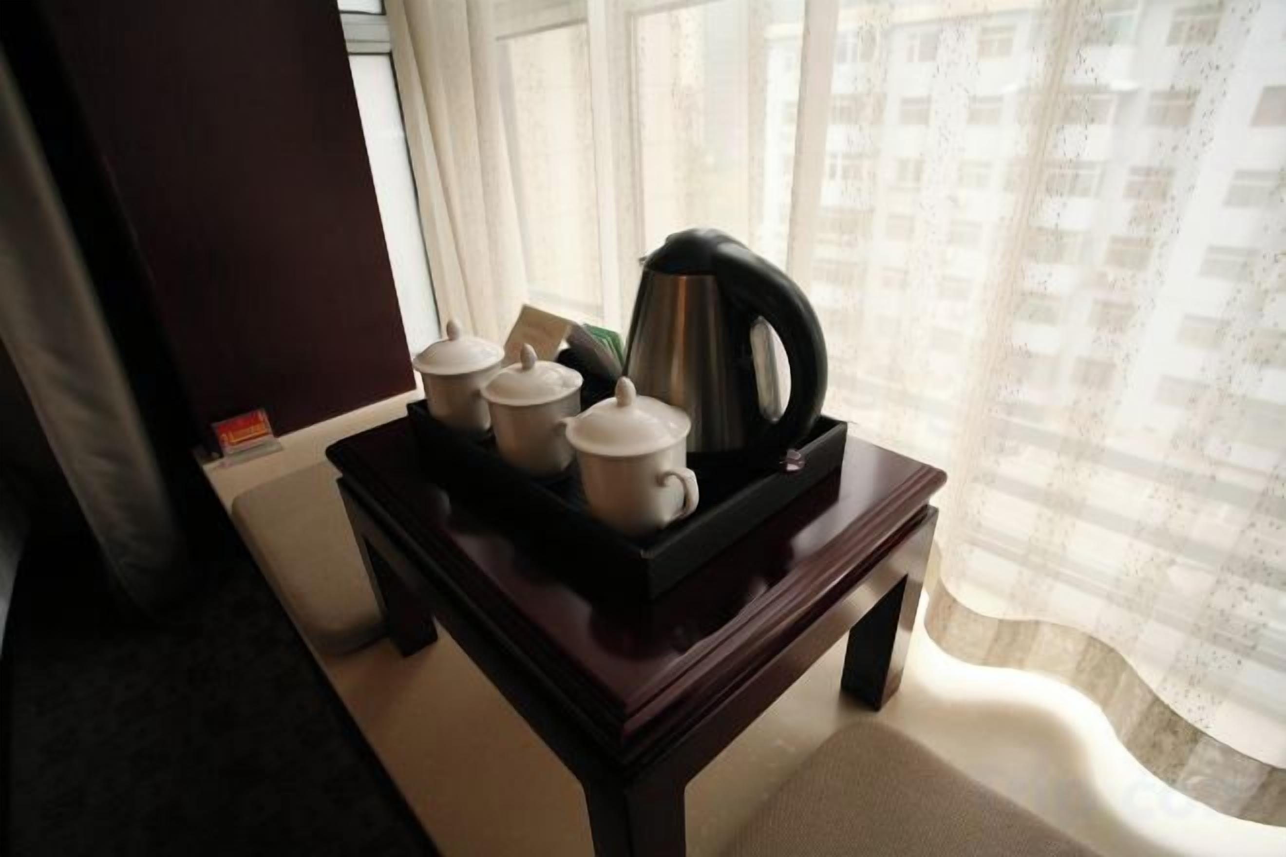 A small table with a tray containing a teapot, cups, and a box, positioned near a window with a curtain.