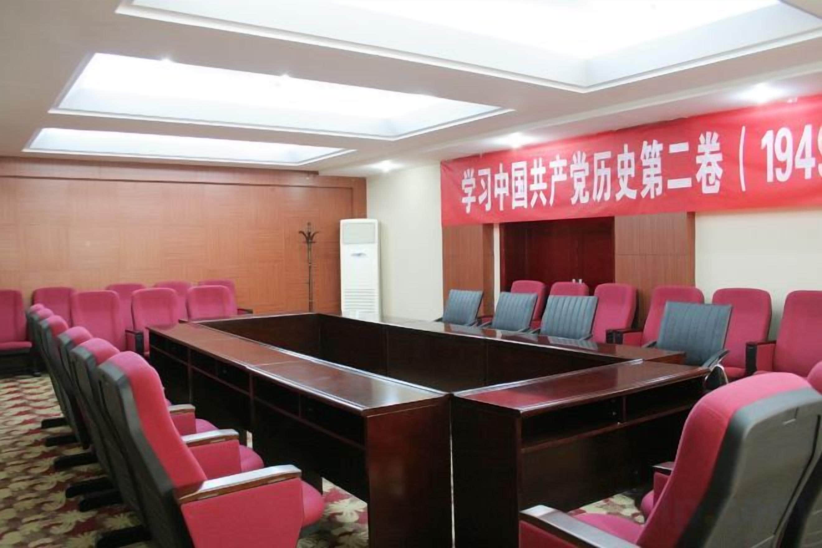 A conference room with a long table and multiple chairs, a red banner with text, and a ceiling light fixture.