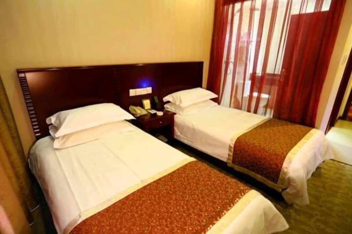 A hotel room with two beds, a nightstand with a phone, and a window with curtains.