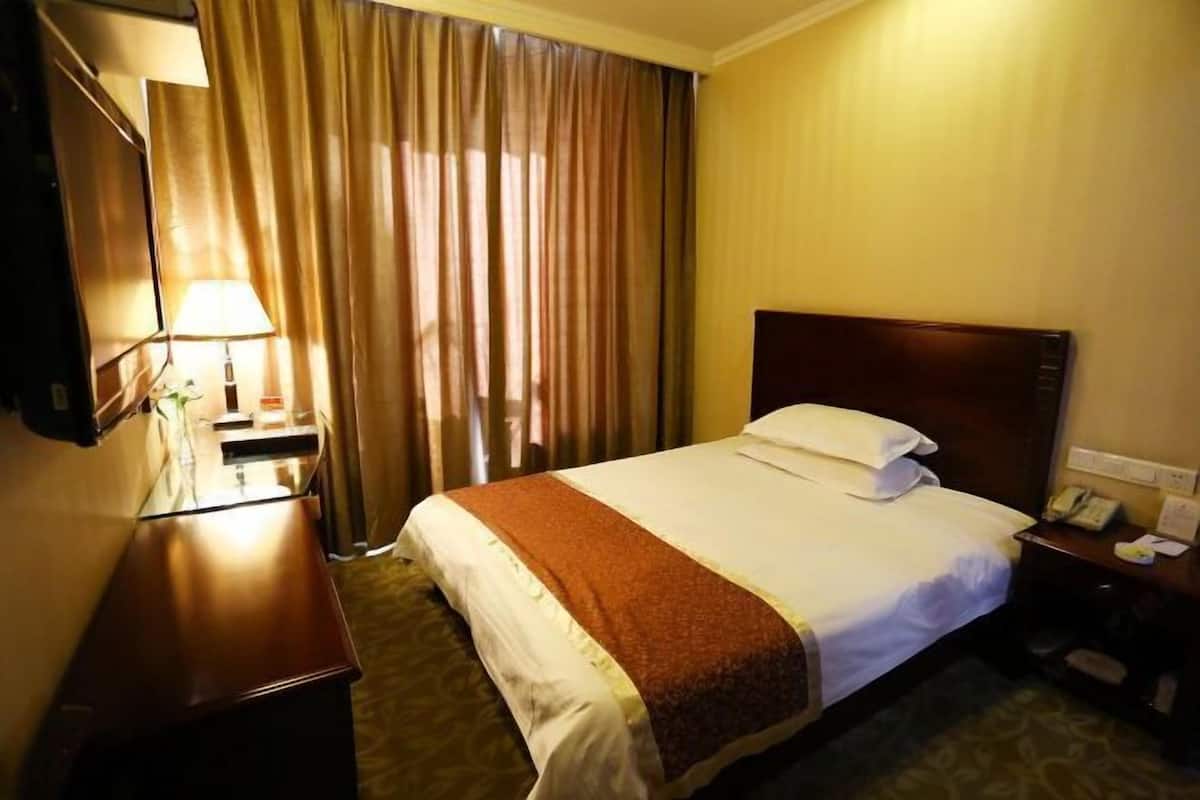 A hotel room with a bed, a desk, a lamp, a telephone, and a window with curtains.