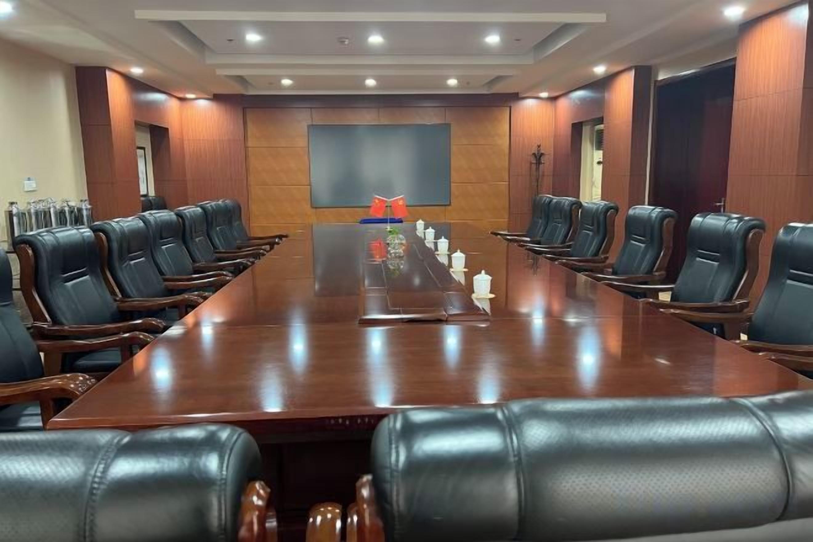 A conference room with a long table, multiple chairs, and a large screen.