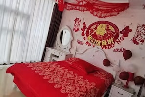 A bedroom with a red bedspread, a mirror, a dresser, and a wall with Chinese New Year decorations. - Shanxi Meitan Hotel (Taiyuan)