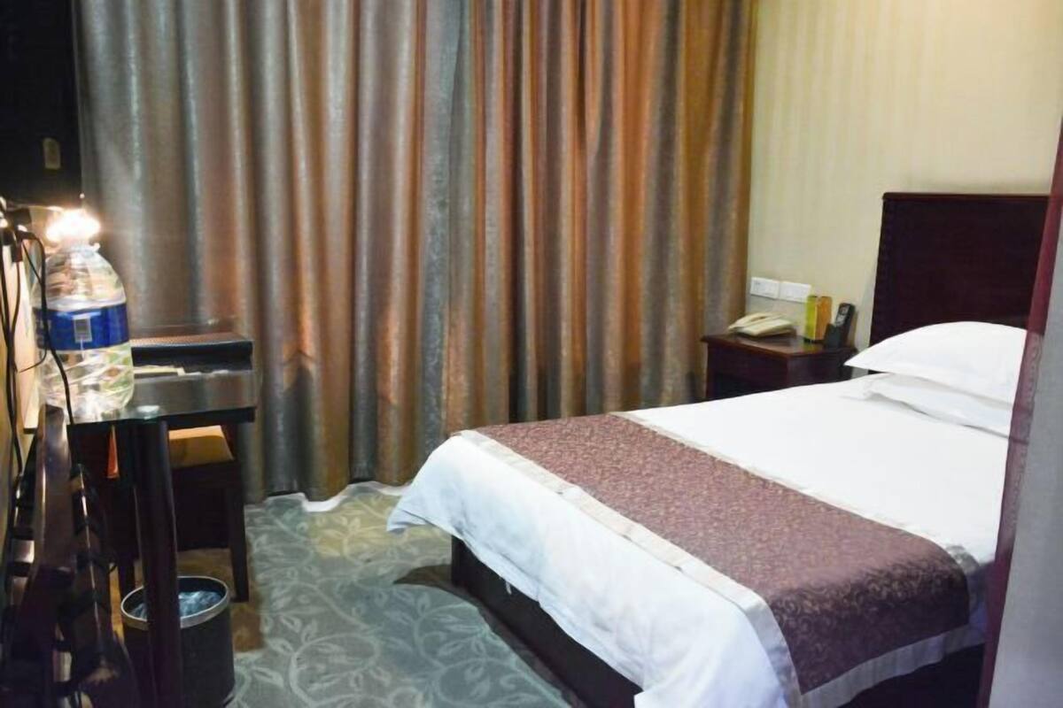 A hotel room with a bed, a desk with a lamp, a telephone, and a water bottle.