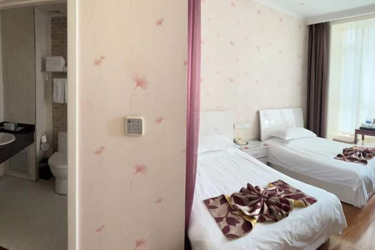 A hotel room with two beds, a bathroom, and a window with curtains.