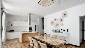 A modern kitchen with white cabinets, a central island, and a dining area with a wooden table and chairs. - 【Villa lamer】 Deluxe Sea View Villa (Koh Samui)