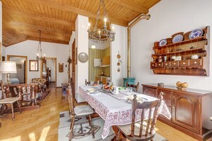 Un comedor con una larga mesa, sillas, una araña y un aparador de madera con platos decorativos.