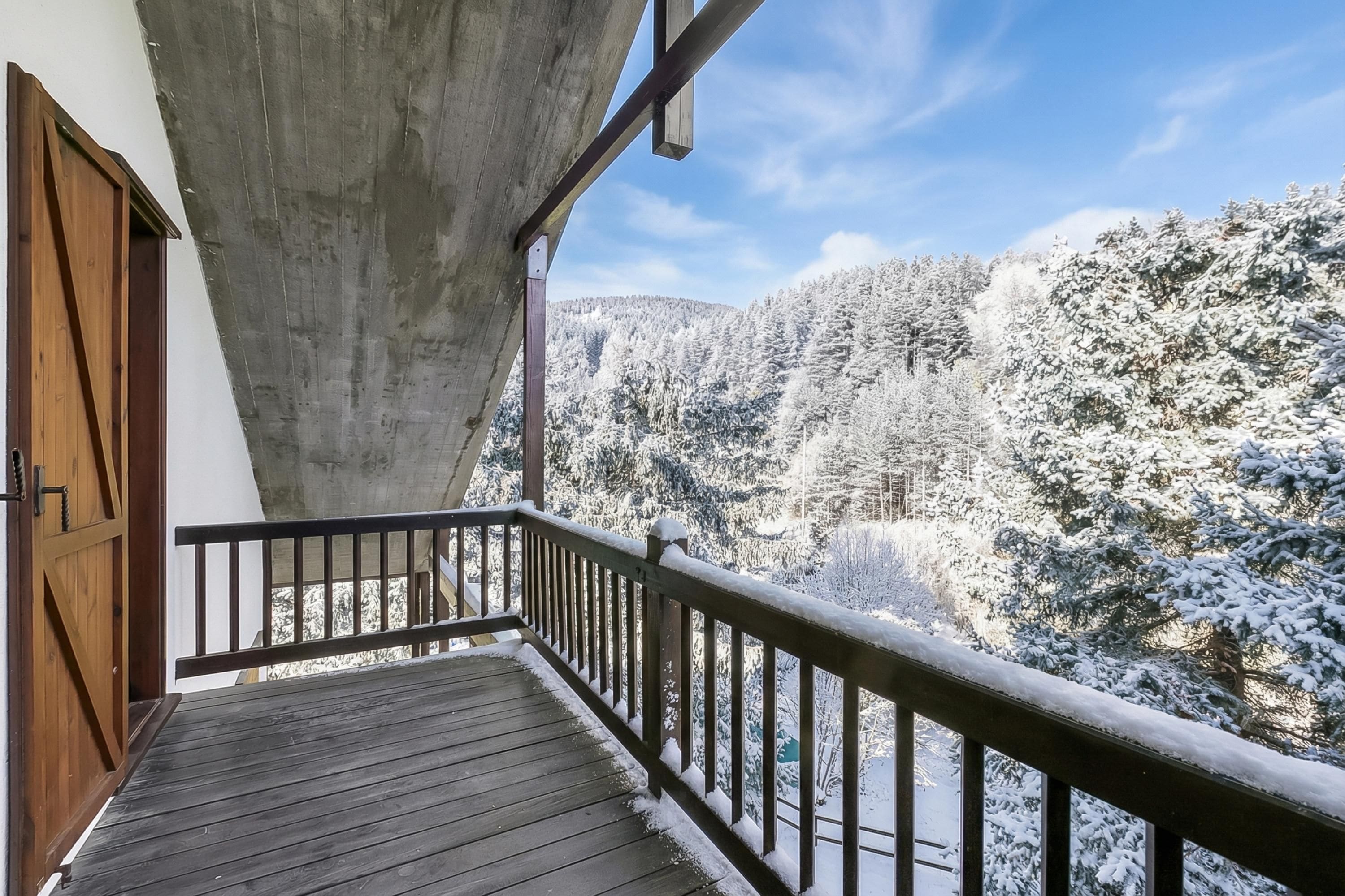 A wooden deck with a metal railing overlooking a snow-covered forest.