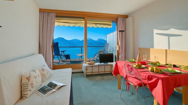 A hotel room with a balcony, a dining table set with plates and glasses, a sofa with a book, and a TV on a stand. - La Casa Di Mitti With View Balcony Near Ski Slopes (Cesana Torinese)