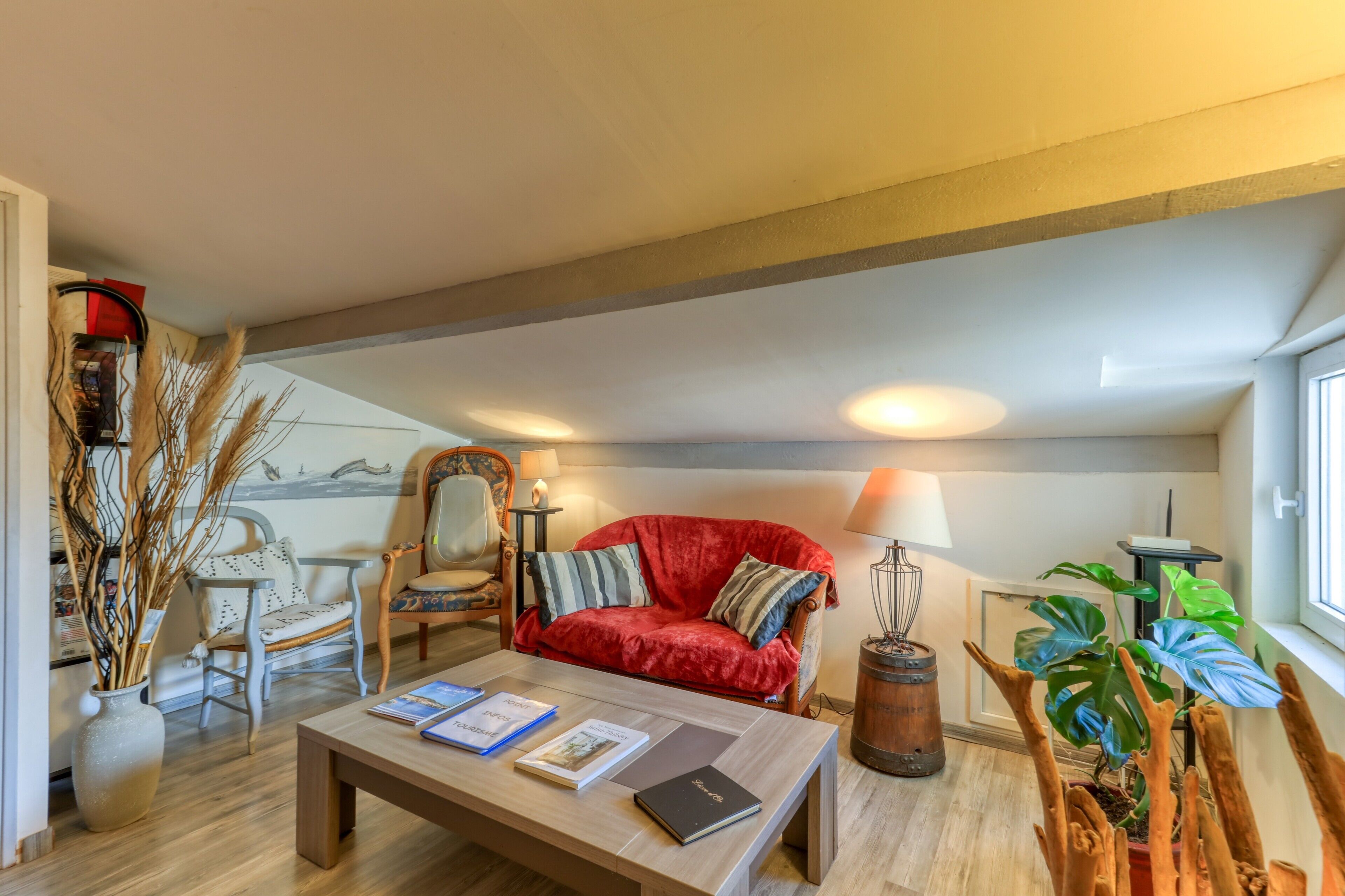 Una sala de estar acogedora con un sofá rojo, una mesa de centro de madera con libros, una lámpara y una planta.