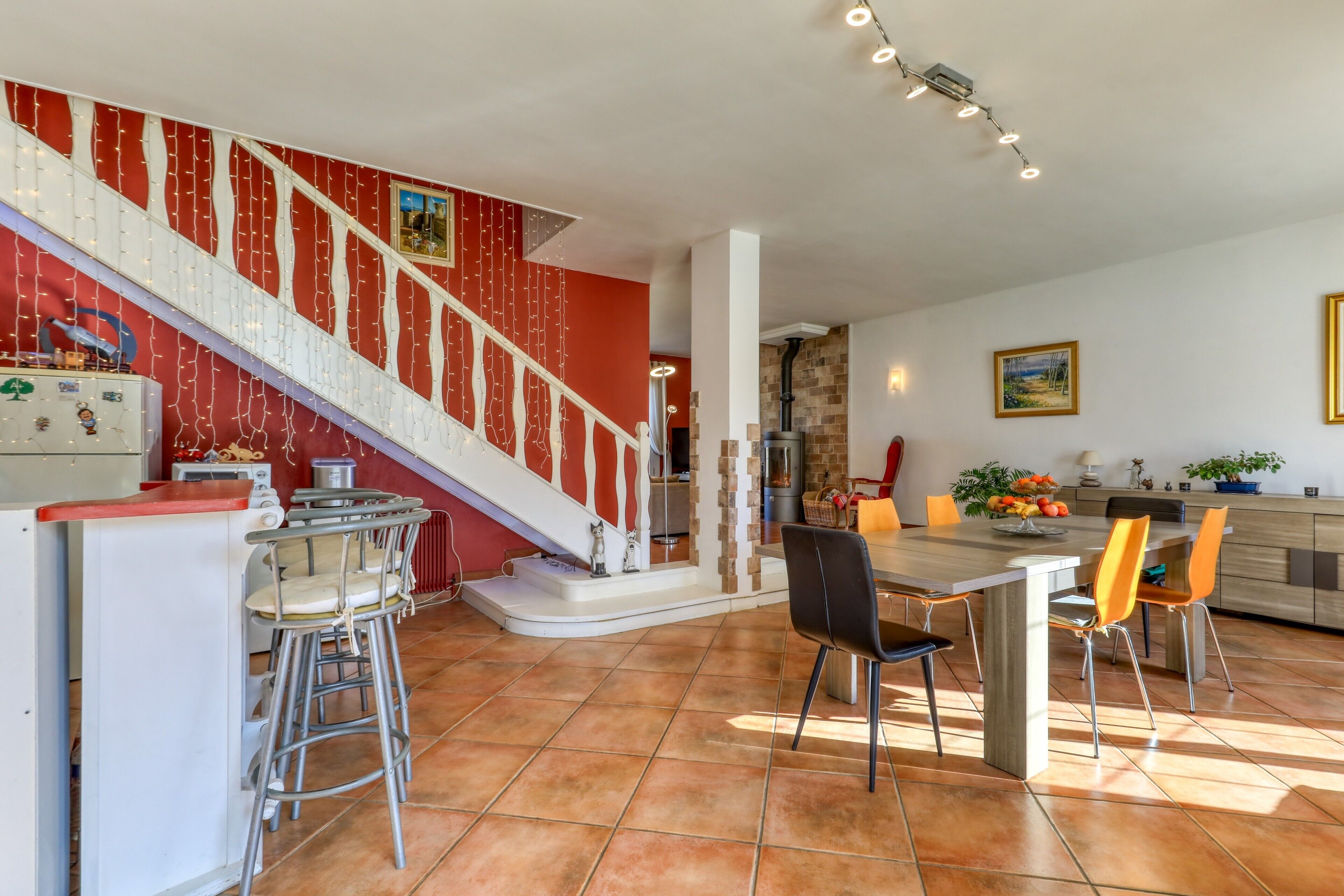 Une cuisine spacieuse avec un coin repas, un escalier décoré de guirlandes lumineuses et un îlot central.