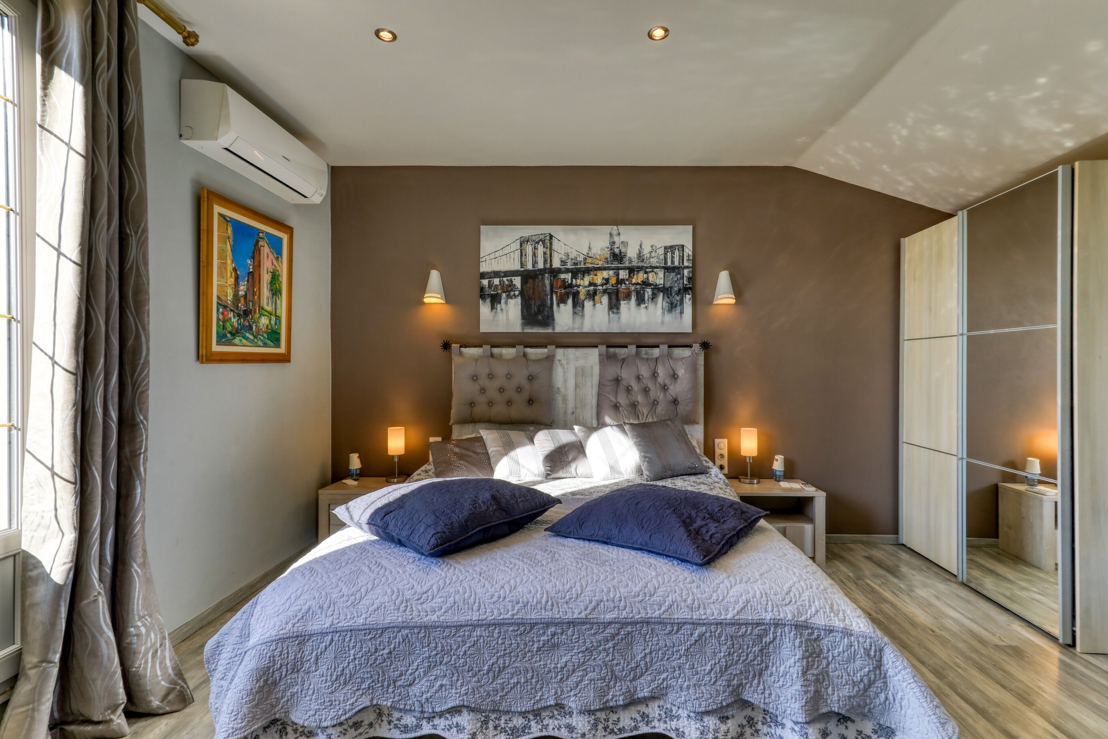 Une chambre à coucher comprenant un lit, des tables de chevet, un tableau, un climatiseur et une armoire.