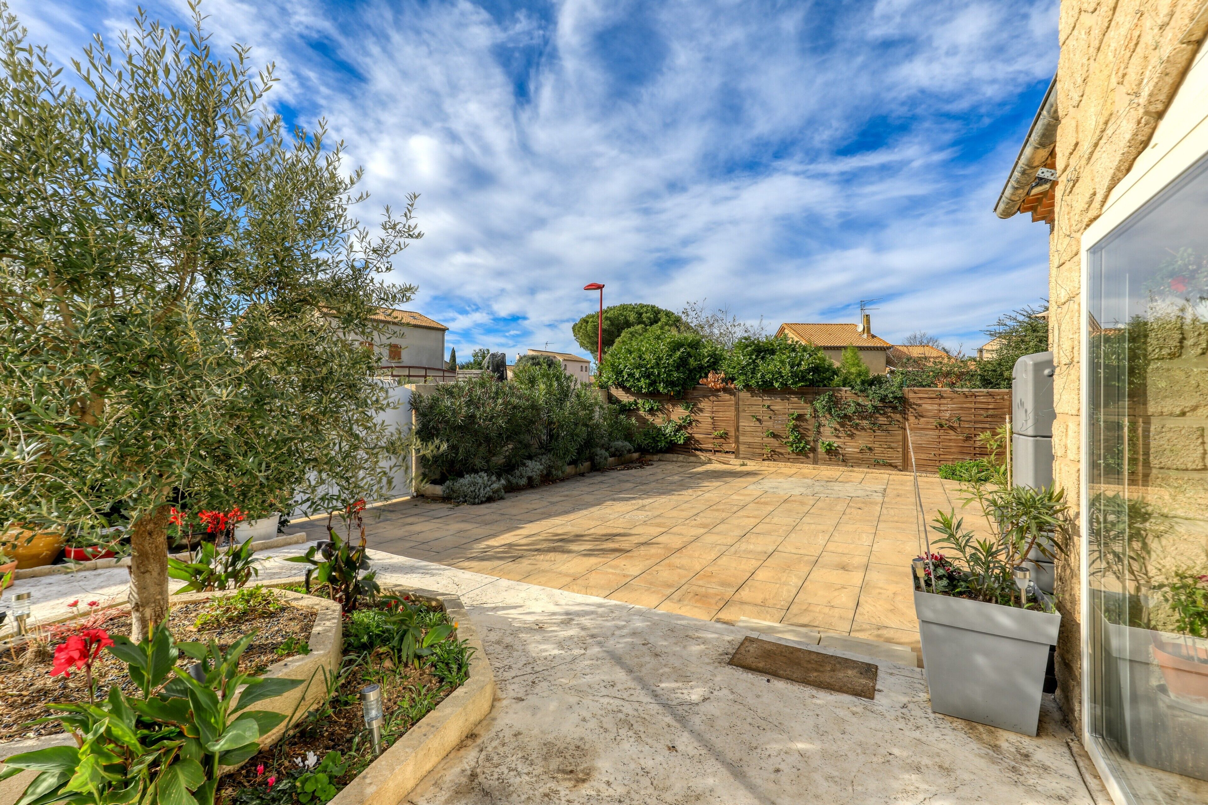 A residential backyard with a paved patio, potted plants, and a wooden fence.
