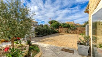 A residential backyard with a paved patio, potted plants, and a wooden fence.