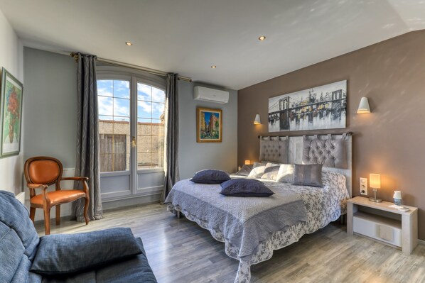 A bedroom with a bed, a chair, a nightstand, a lamp, and a window.
