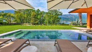 A swimming pool with lounge chairs and umbrellas, surrounded by greenery and a mountain view. - Lakefront Serenity Villa With Pool (Mandello del Lario)