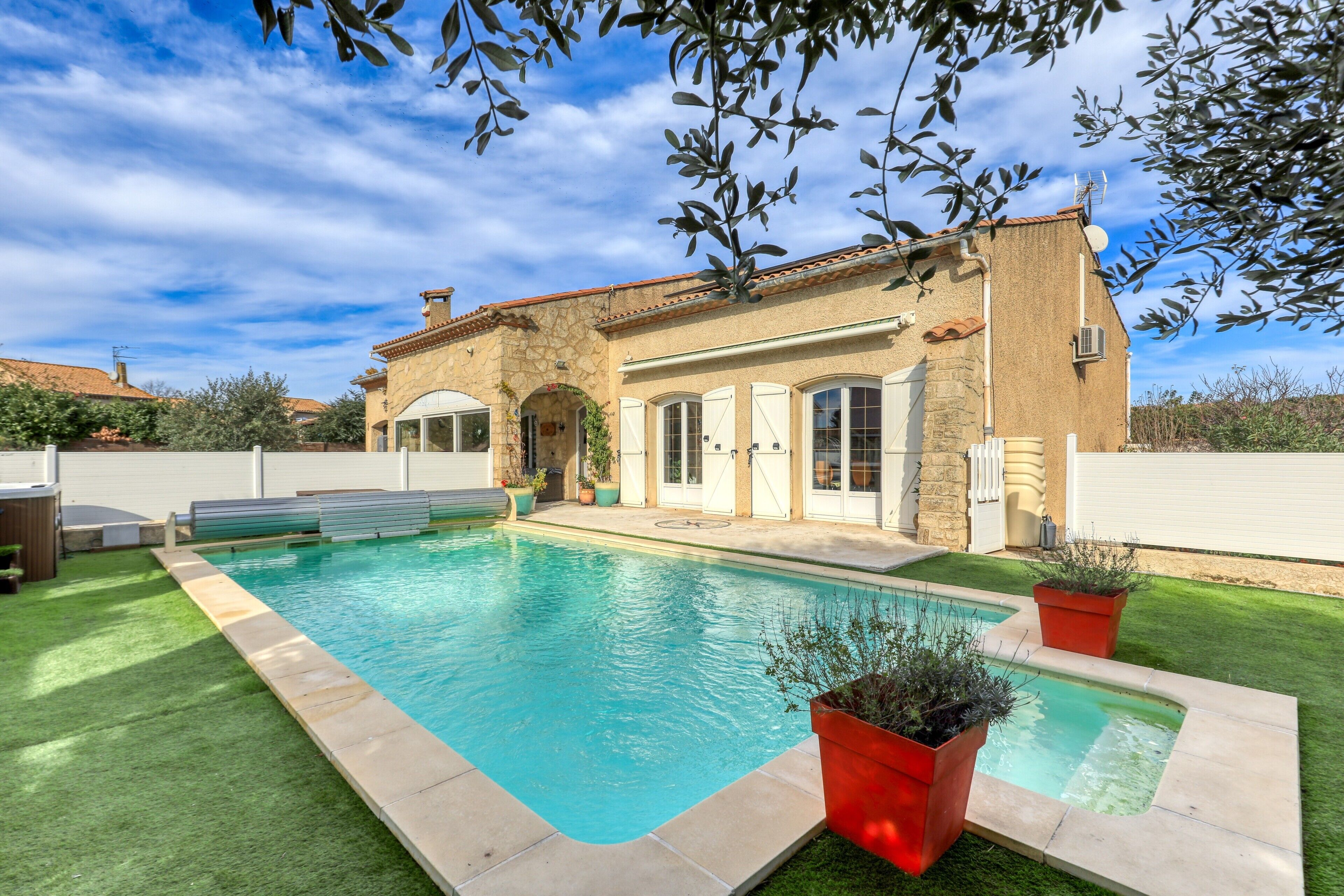A house with a swimming pool, a stone facade, and a well-maintained lawn.