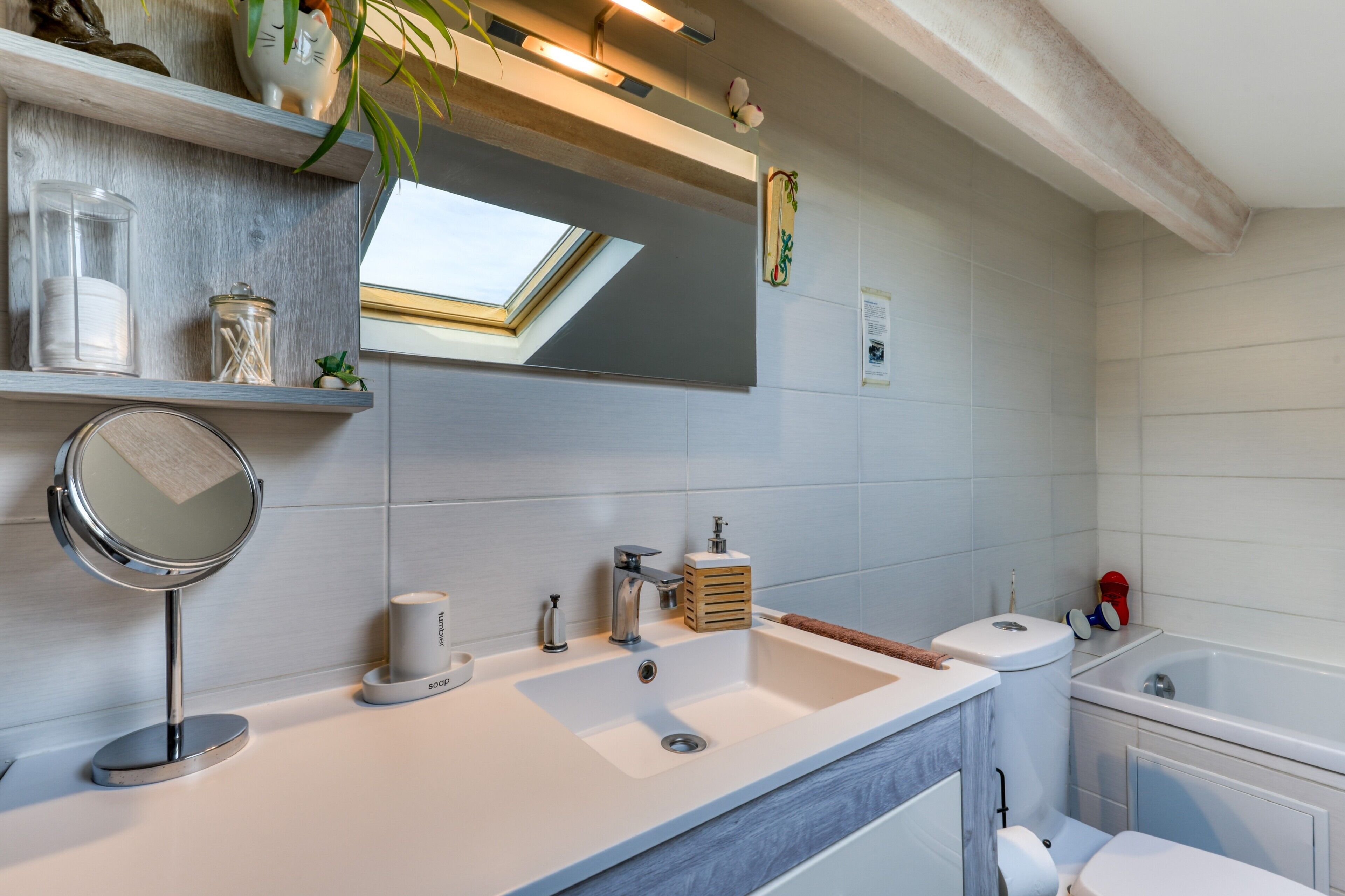A modern bathroom with a large mirror, a sink, a toilet, and a bathtub.