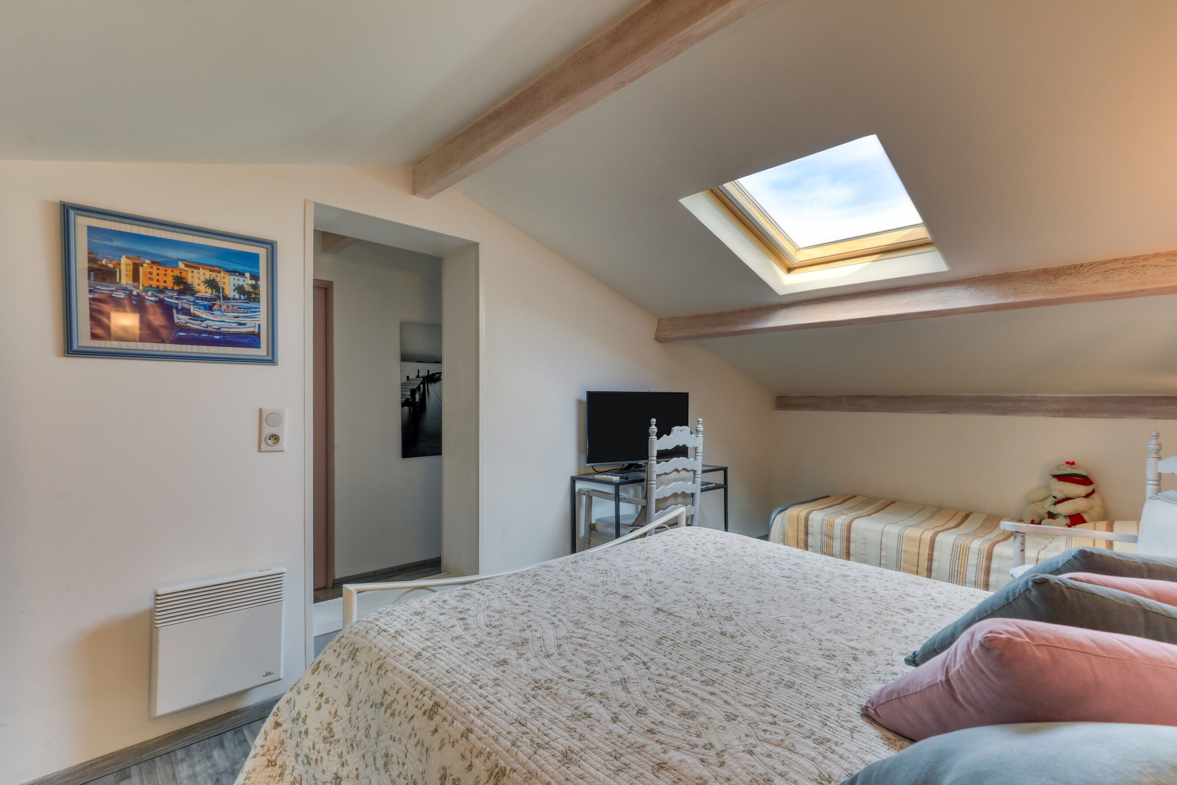 Ein Schlafzimmer mit Dachfenster, einem Bett mit gemusterten Betttextilien, einem Fernseher und einem gerahmten Bild an der Wand.