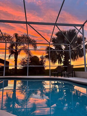 A pool area with a sunset view, surrounded by palm trees and a metal structure. - 25 Min to Disney! Highlands Residence – 5BR Pool Villa w/ Golf Views (Davenport)