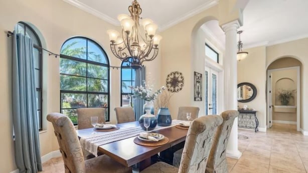 A dining room with a large table, chairs, a chandelier, and large windows.