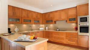 A modern kitchen with wooden cabinets, stainless steel appliances, and a central island with a fruit bowl. - Samar Villa, centrally located, close to the beach, A/C, option of fenced pool (Santanyí)