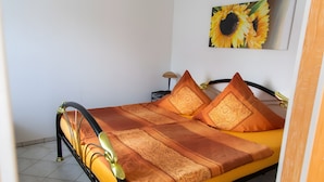 A bed with a patterned bedspread and pillows, a nightstand with a lamp, and a sunflower painting on the wall. - Holiday Home 'Stahlberg' with Private Terrace, Balcony and Wi-Fi (Potsdam)