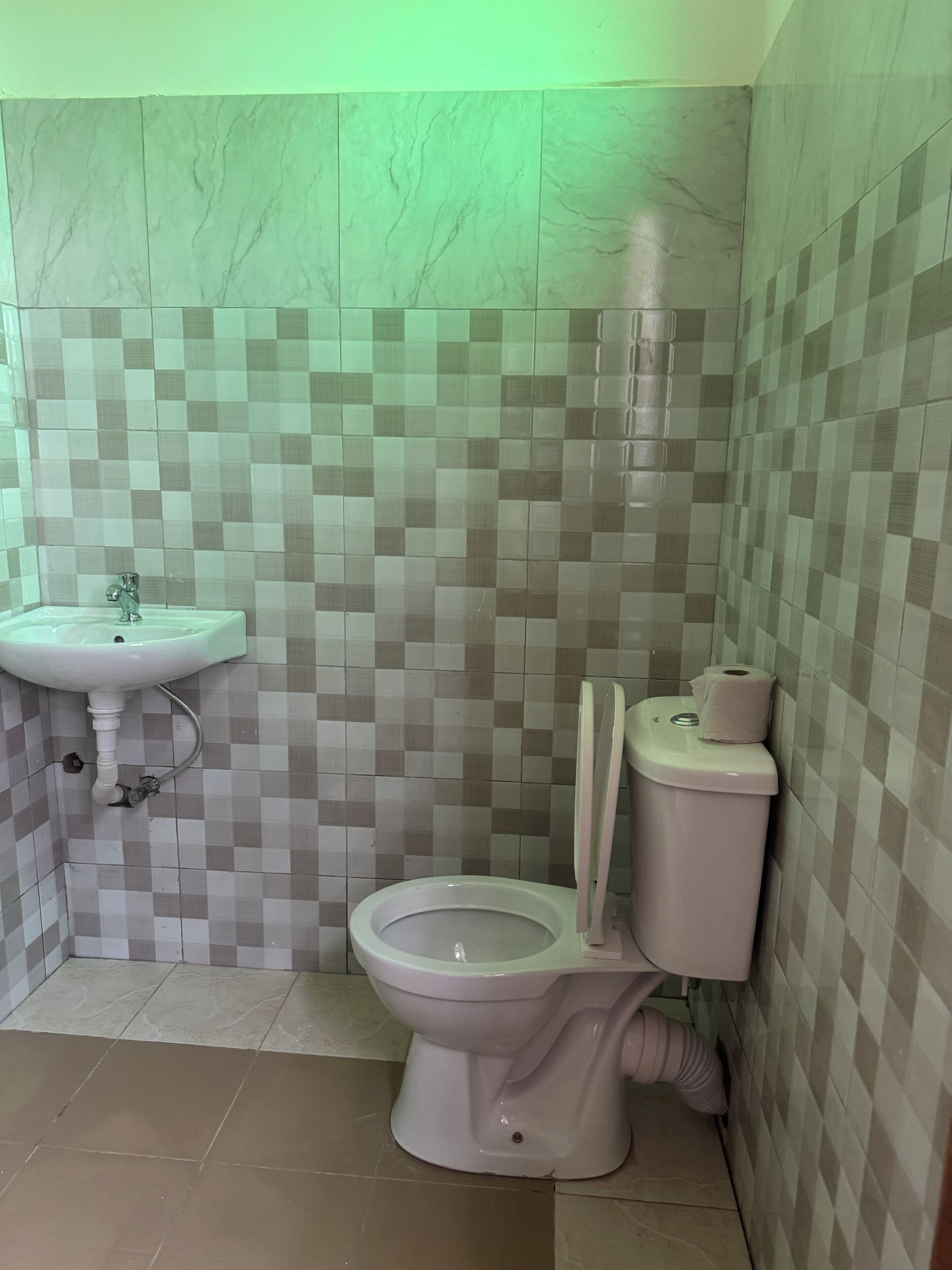 Et badeværelse med toilet, vask og flisebeklædte vægge.