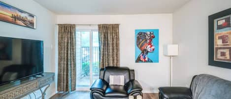 Ein Wohnzimmer mit Fernseher, einer Couch, einem Sessel und einem Bild an der Wand.