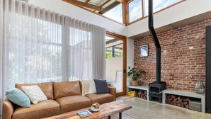 A modern living room with a brown leather sofa, a wooden coffee table, and a brick fireplace. - 'The Foundry' Modern Industrial Home w/Courtyard & Fireplace, Adelaide CBD (Adelaide)