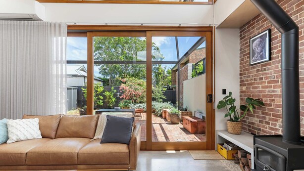 A modern living room with a leather sofa, a fireplace, and a sliding glass door leading to a backyard. - 'The Foundry' Modern Industrial Home w/Courtyard & Fireplace, Adelaide CBD (Adelaide)