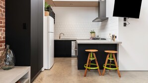 A modern kitchen with a TV, two stools, and a brick wall. - 'The Foundry' Modern Industrial Home w/Courtyard & Fireplace, Adelaide CBD (Adelaide)