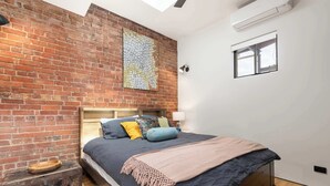 A bedroom with a brick wall, a map artwork, a bed with pillows, a wooden headboard, a small window, and a ceiling fan. - 'The Foundry' Modern Industrial Home w/Courtyard & Fireplace, Adelaide CBD (Adelaide)