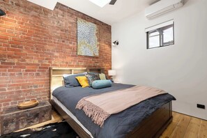 A bedroom with a brick wall, a map artwork, a bed with pillows, a wooden headboard, a small window, and a ceiling fan. - 'The Foundry' Modern Industrial Home w/Courtyard & Fireplace, Adelaide CBD (Adelaide)