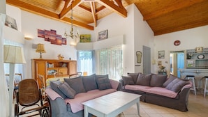Ein geräumiges Wohnzimmer mit hoher Decke, Holzbalken, einem großen Sofa, einem Couchtisch und einem Essbereich mit Stühlen und einem Tisch.