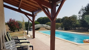 Ein überdachter Außenbereich mit Pool, Liegestühlen und einer Pergola.