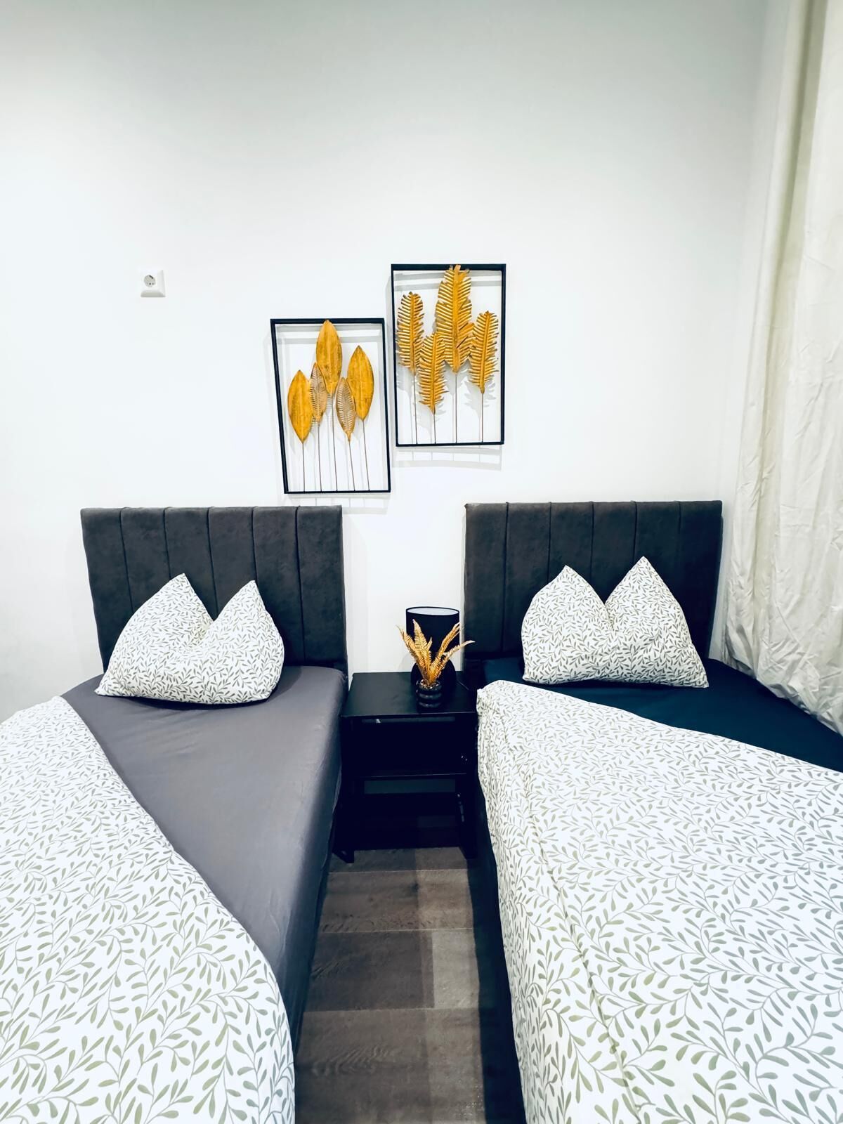 Habitación doble con dos camas, cada una con una colcha estampada y cojines a juego. Encima de las camas hay láminas botánicas enmarcadas.