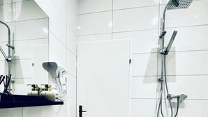 Moderni kylpyhuone, jossa on valkoiset laatat, marmorilattia, pesuallas, peili, suihku ja ovi.
