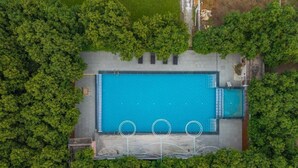 An aerial view of a rectangular swimming pool surrounded by dense greenery, with a paved deck and a few seating areas. - GIR VIHAR RESORT (Talala)