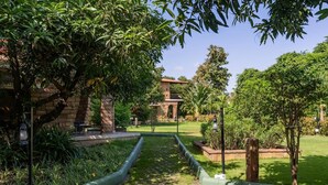 A garden pathway leading to a building with a brick facade and a balcony. - GIR VIHAR RESORT (Talala)
