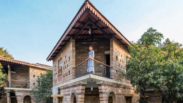 A stone building with a balcony, arched doorways, and a wooden staircase leading to the entrance. - GIR VIHAR RESORT (Talala)