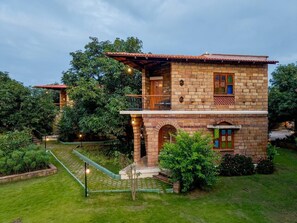 Une maison en pierre à deux étages, dotée d’un balcon, entourée d’une végétation luxuriante et d’un jardin bien entretenu.