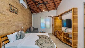 A bedroom with a wooden bed, a TV on a wooden stand, and a ceiling fan. - GIR VIHAR RESORT (Talala)