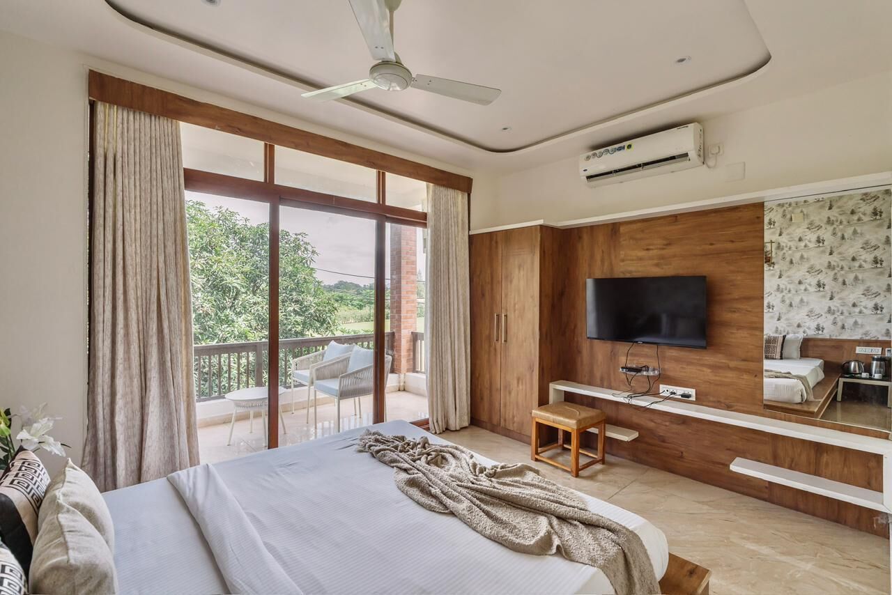 Ein Schlafzimmer mit Bett, Fernseher, Schreibtisch und einem Balkon mit Blick auf Grünflächen.