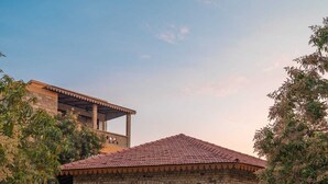 A stone archway leading to a covered outdoor dining area with a tiled roof, surrounded by greenery and a paved walkway. - GIR VIHAR RESORT (Talala)