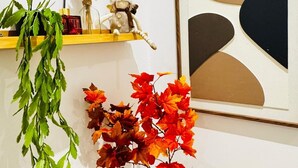 Habitació amb una estant de fusta on hi ha un objecte decoratiu, un vas amb fulles d'octubre i una obra d'art abstracta emmarcada.