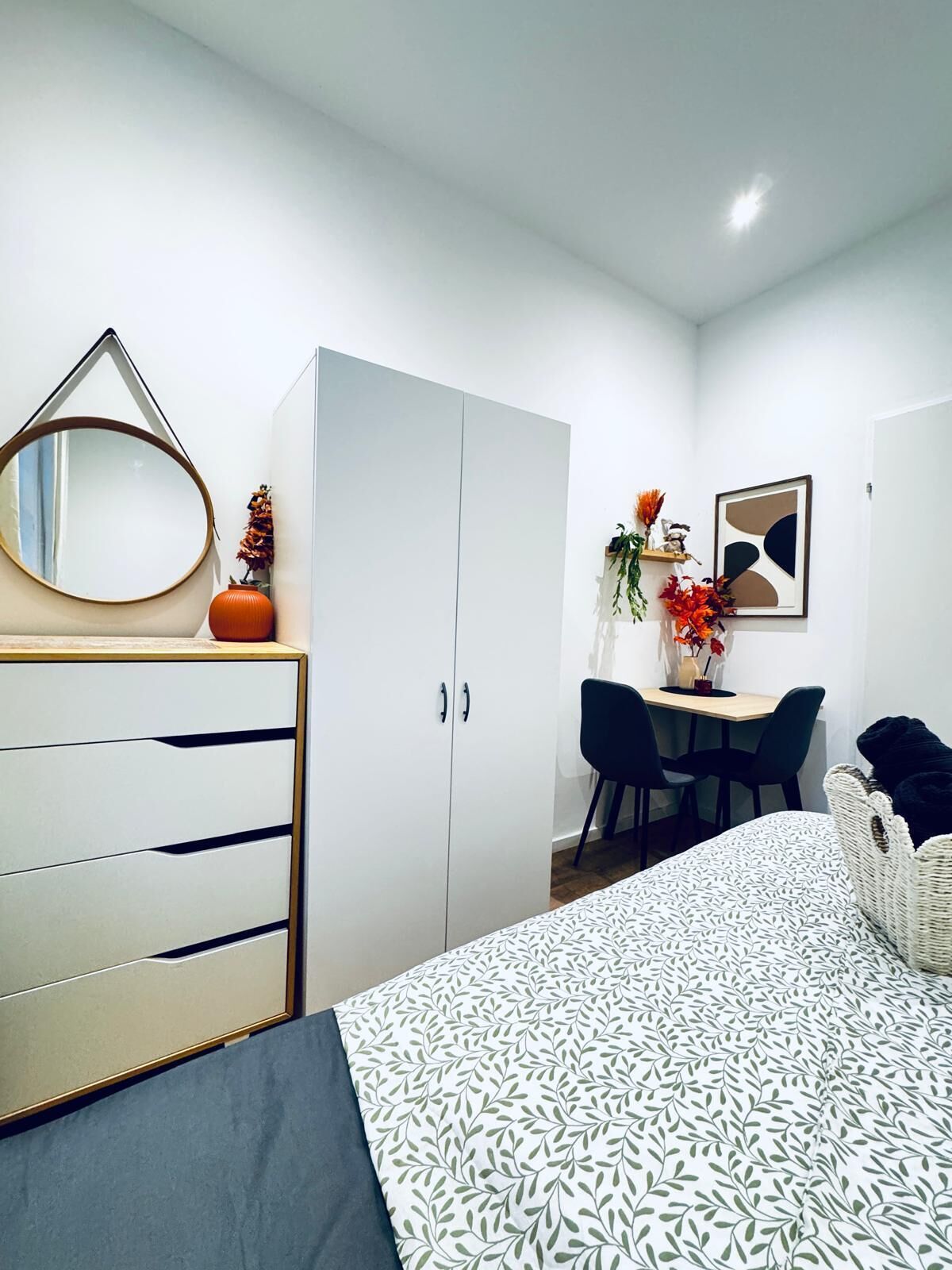 Quarto moderno com cama, cômoda, escrivaninha e cadeiras.