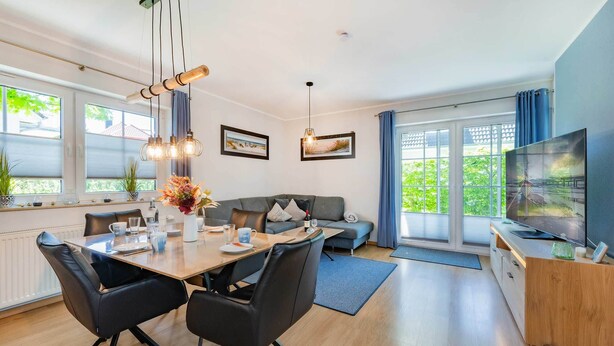 A modern living room with a dining area, a sofa, a TV, and large windows. - Comfortable vacation apartment in Koserow with terrace and modern furnishings (Koserow)