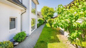 A white building with a paved walkway, green shrubs, and a tree. - Comfortable vacation apartment in Koserow with terrace and modern furnishings (Koserow)