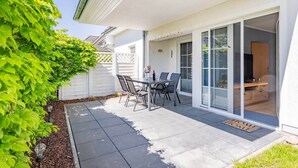 A patio with a table and chairs, a sliding glass door, and a white fence. - Comfortable vacation apartment in Koserow with terrace and modern furnishings (Koserow)