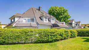 A large house with multiple levels, a prominent chimney, and a well-maintained hedge in the foreground. - Comfortable vacation apartment in Koserow with terrace and modern furnishings (Koserow)